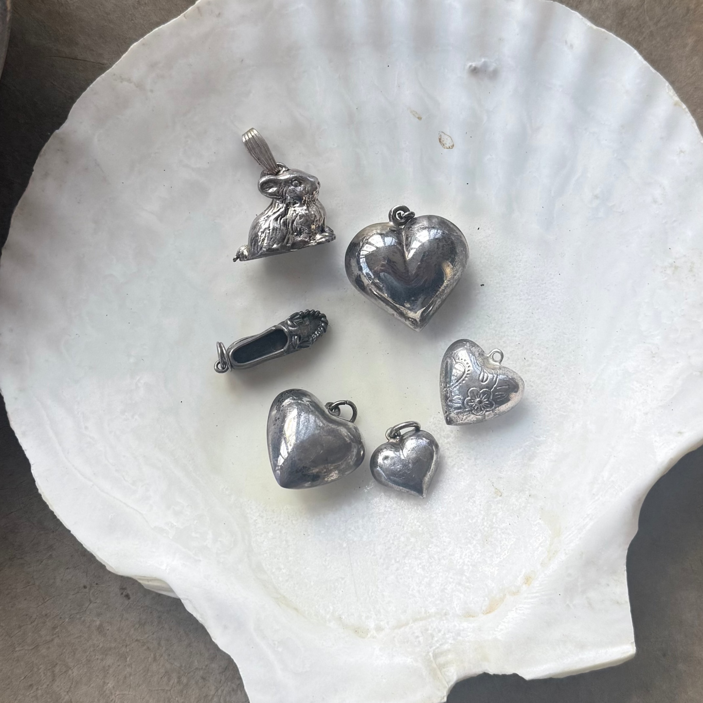 Silver jewelry charms on a shell with a metal container next to it on a concrete surface